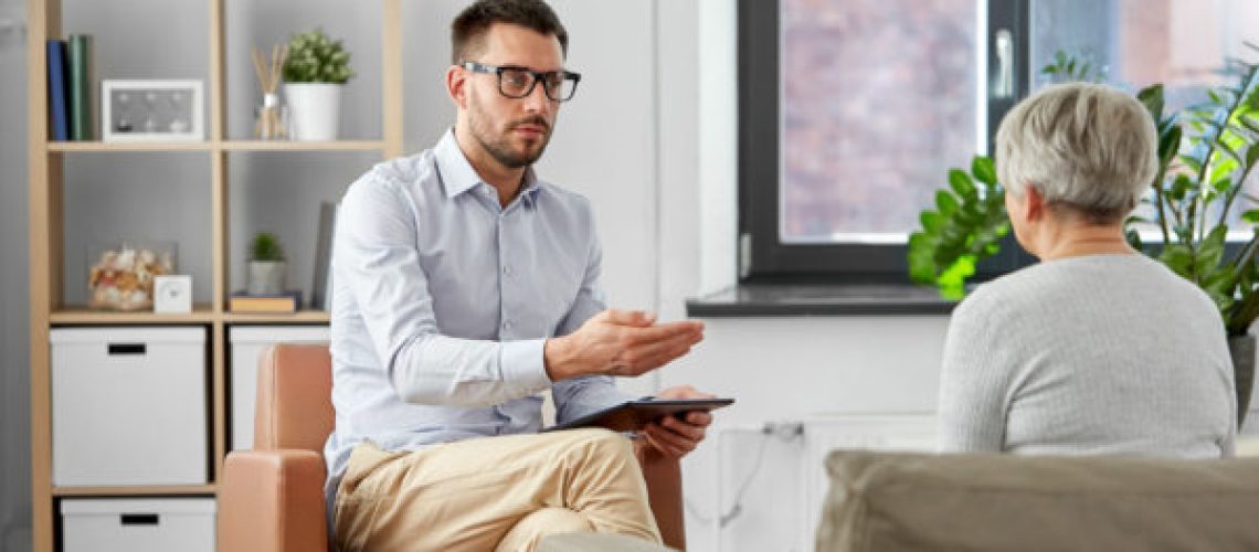 geriatric psychology, mental therapy and old age concept - psychologist with tablet computer talking to to senior woman patient at psychotherapy session